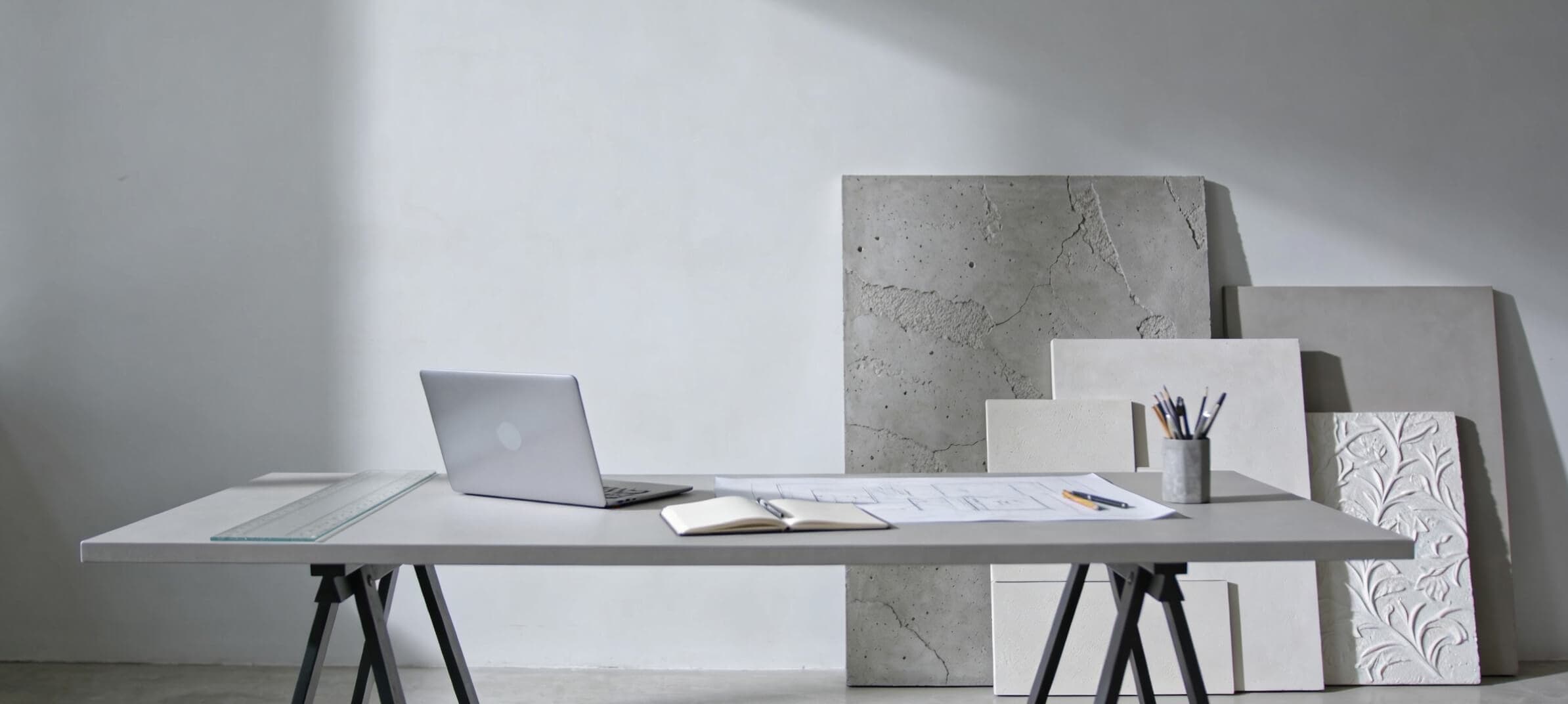 Birou de arhitectură cu planuri, laptop și plăci de probă cu tencuieli decorative sprijinite de perete
